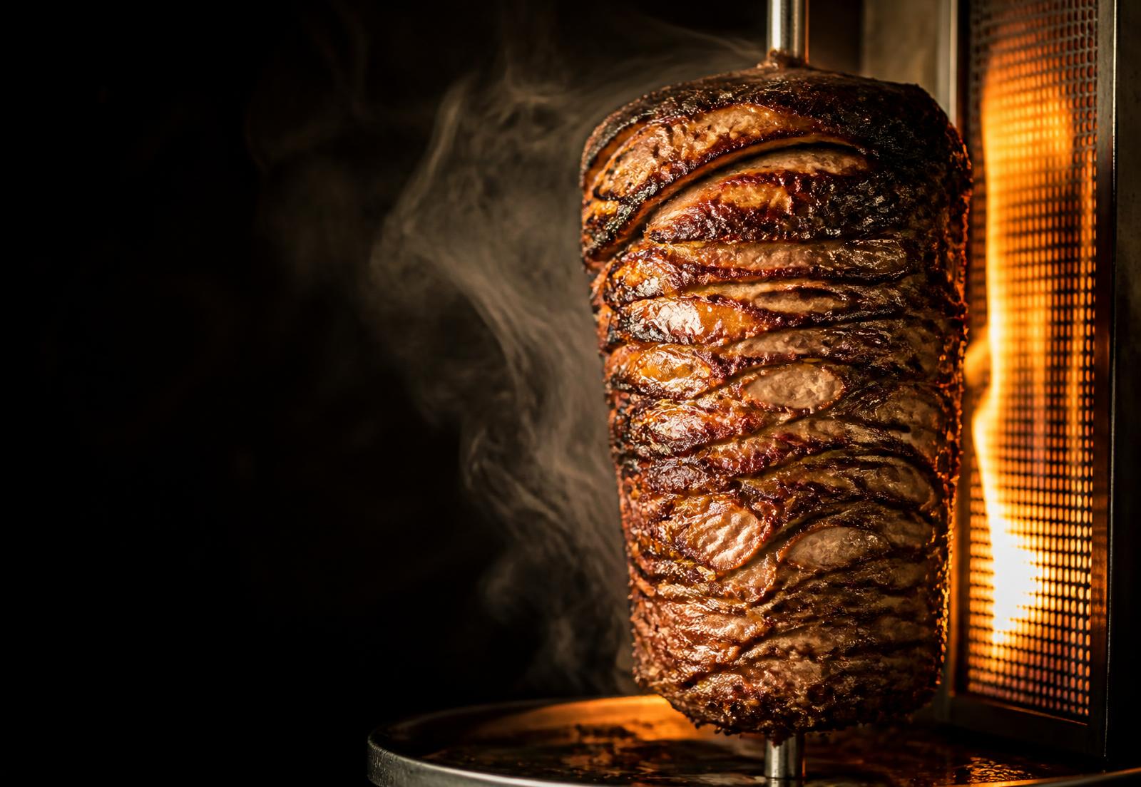 Beef shawarma roasting on a vertical spit over an open flame